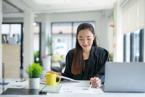 Free Download Asian businesswoman analyzing financial charts and business documents, working with laptop computer at modern office - GFXLoad