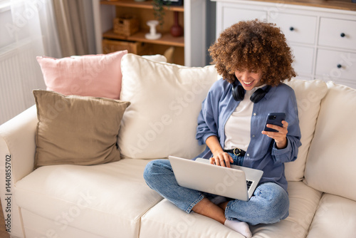 Relaxed African American Woman In Denim Working From Home With Multiple Devices On Cozy White Sofa