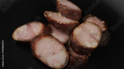 Slices of smoked sausage arranged on a dark plate amidst a rustic kitchen setting at twilight