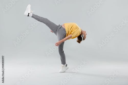 Girl with headphones in stylish clothes dancing on light grey background