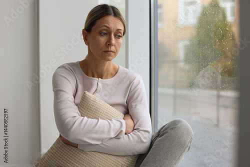 Depressed woman looking out window at home, space for text