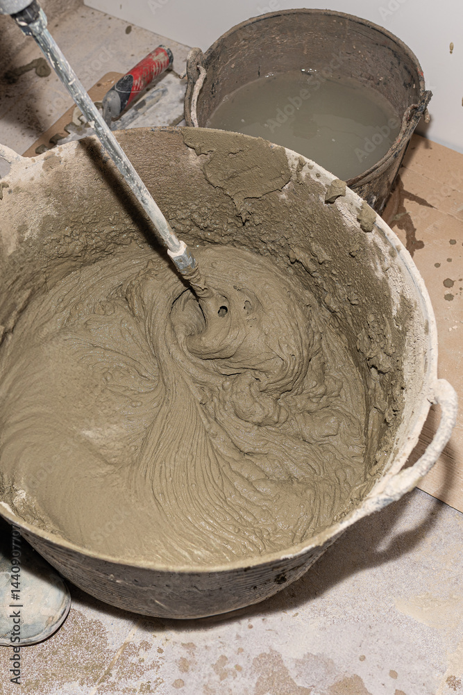 Fototapeta premium Construction worker mixing cement in bucket using mixing paddle attached to electric drill