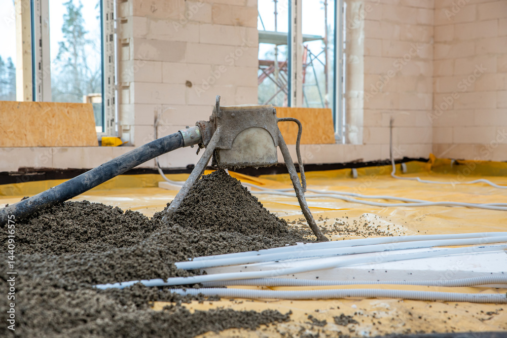 A construction site showing a concrete pump discharging onto a yellow sheet, white conduit pipes in the foreground, and scaffolding around white block walls.