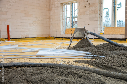 Obraz na płótnie An under construction interior with light brick walls, concrete pouring via a hose, yellow floor covering, white pipes, and large windows with scaffolding outside. w salonie