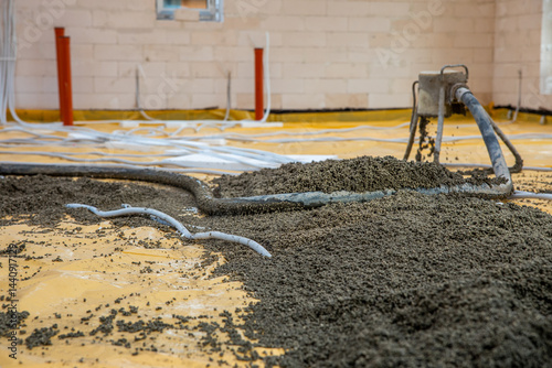 Obraz na płótnie Concrete pouring process on yellow protective sheet in a construction site interior. Red pipes, white tubing, and light brick walls are visible. w salonie