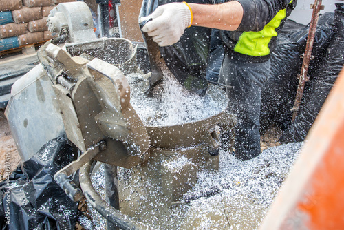 A worker in high visibility gear pours white granules into a concrete mixer surrounded by black coverings and construction materials at an active site.