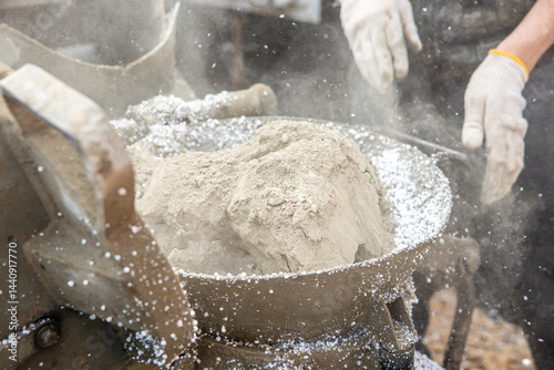 Obraz na płótnie Powdered material and white granules mix in a metal container, with gloved hands nearby. Dust particles are visible, indicating an industrial process. w salonie