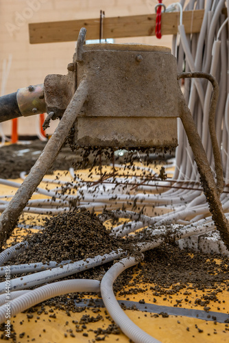 Obraz na płótnie A construction site shows a machine spreading gravel on a yellow sheet covered floor, surrounded by white tubes, wooden beams, and tools in progress. w salonie