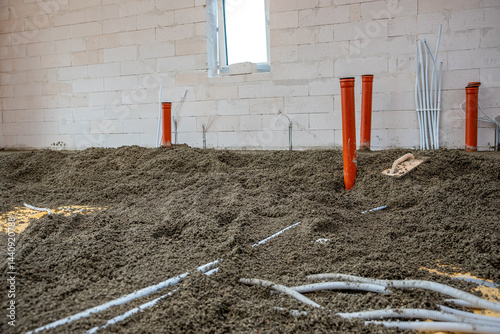 Obraz na płótnie Interior under construction with gravel flooring, orange pipes, white conduits, concrete block walls, and a window opening allowing light inside. w salonie
