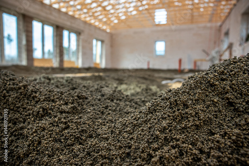 Obraz na płótnie Construction site showing an exposed wooden roof framework, unfinished walls with large window openings, and granular material spread on the floor. w salonie