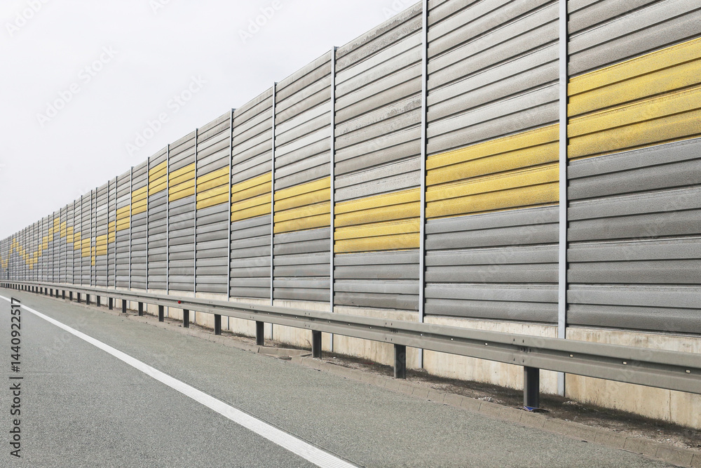 Modern highway sound barrier. Long noise protection wall. Urban infrastructure design. Gray and yellow panels. Roadside safety concept. Contemporary architectural structure. Silent travel environment.