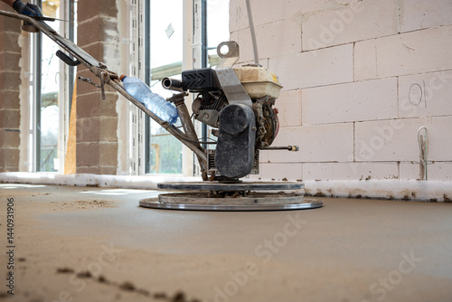 Obraz na płótnie A power trowel machine smooths fresh concrete flooring in an unfinished interior with exposed brick walls, large windows, and underfloor heating pipes. w salonie