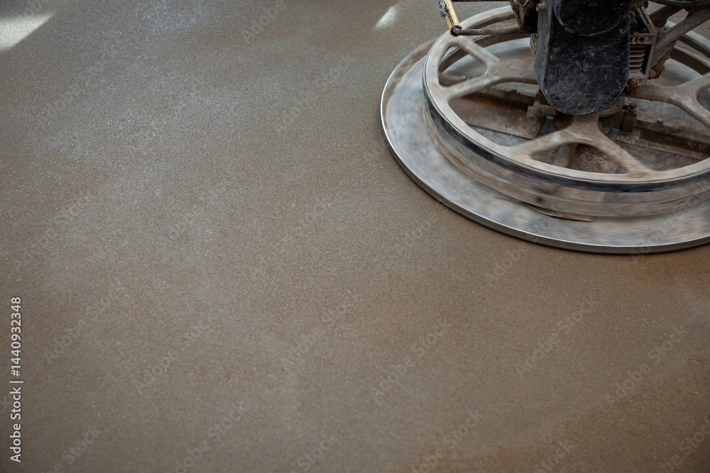A power trowel machine with a circular metal blade polishes a freshly laid concrete floor, emphasizing texture and sheen under focused lighting.
