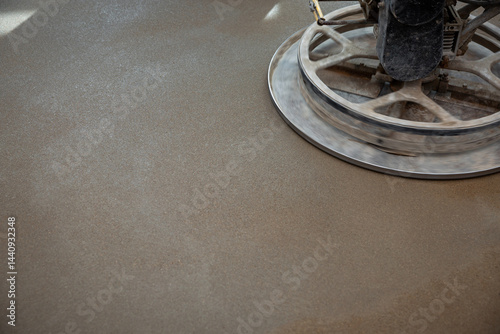 Obraz na płótnie A power trowel machine with a circular metal blade polishes a freshly laid concrete floor, emphasizing texture and sheen under focused lighting. w salonie
