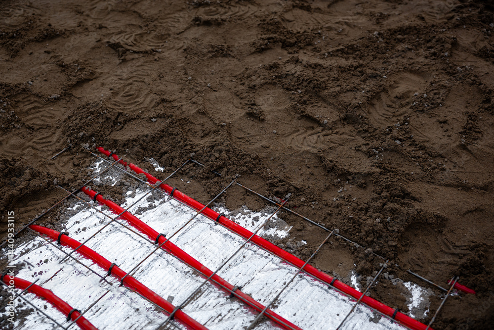Underfloor heating pipes arranged on reflective insulation, secured by a metal grid, with soil preparation for Estrich concrete visible on the surface.