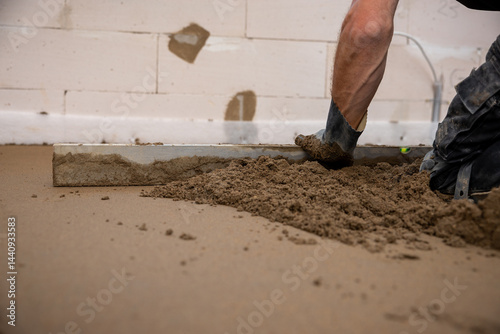Obraz na płótnie A worker uses a leveling tool to smooth Estrich concrete over underfloor heating pipes. Partially finished walls and exposed material are visible indoors. w salonie