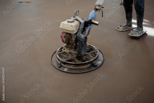 Obraz na płótnie A construction worker smooths wet concrete using a power trowel, revealing embedded underfloor heating pipes. Protective footwear is worn for safety. w salonie