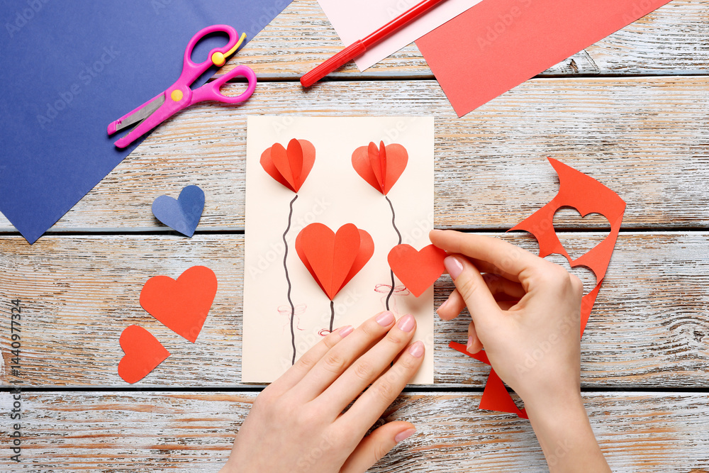 Woman making postcard with hearts at wooden table, top view. Child handmade craft