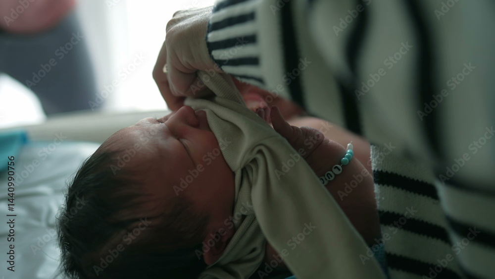 Fototapeta premium Mother tenderly caring for her newborn baby, dressing the baby in clothing, capturing an intimate moment of maternal care and love in a softly lit indoor environment