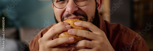 фотографія Man with glasses biting into a large burger with intense enjoyment, captured in close-up