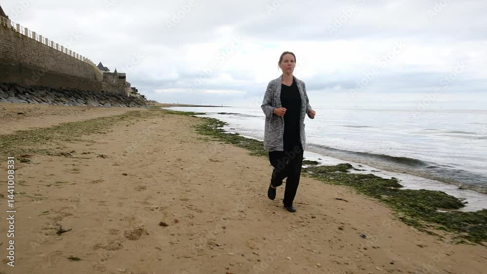 Woman strolling on sandy beach near historic sea wall on overcast day Woman strolling on sandy beach near historic sea wall on overcast day