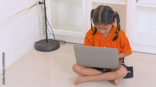 Asian girl sitting on the floor and using laptop computer, studying through online e-learning system, homeschooling, new normal lifestyle, kid and technology concept