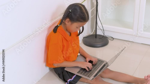 Asian girl sitting on the floor and using laptop computer, studying through online e-learning system, homeschooling, new normal lifestyle, kid and technology concept