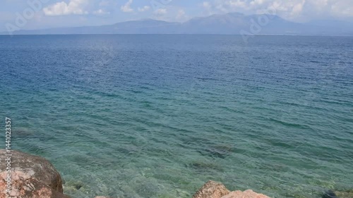 View of Euboea island from opposite coast in Agii Apostoli, showcasing the serene blue waters. The landscape is combination of rocky shores and distant mountains of Evia, creating tranquil atmosphere