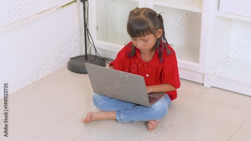 Asian girl sitting on the floor and using laptop computer, studying through online e-learning system, homeschooling, new normal lifestyle, kid and technology concept