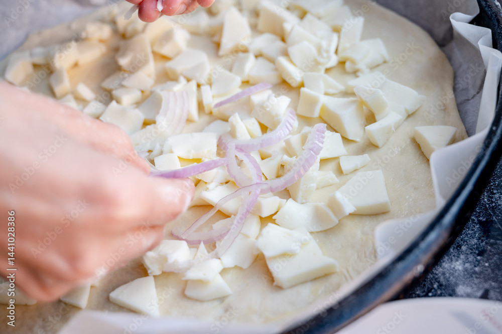 Close-up scene of female hands. Adding onion to dough on kitchen countertop. Making homemade pizza with three types of cheese – female hands in action.