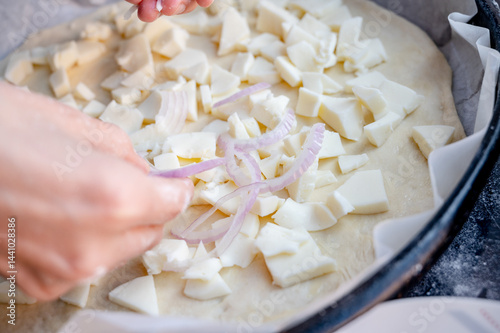 Obraz na płótnie Close-up scene of female hands. Adding onion to dough on kitchen countertop. Making homemade pizza with three types of cheese – female hands in action. w salonie