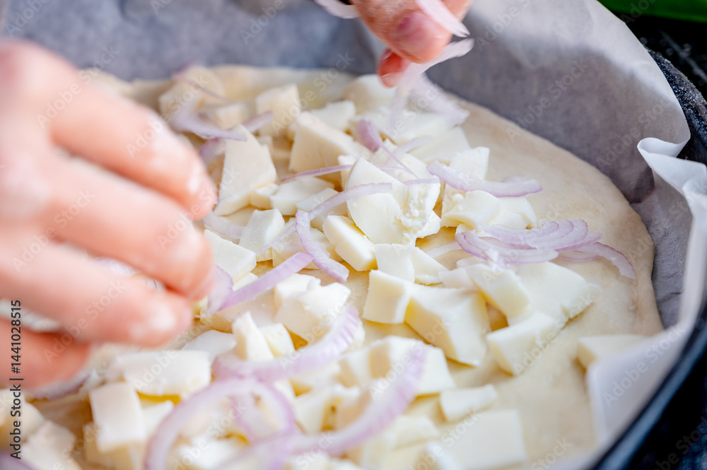 Close-up scene of female hands. Adding onion to dough on kitchen countertop. Making homemade pizza with three types of cheese – female hands in action.