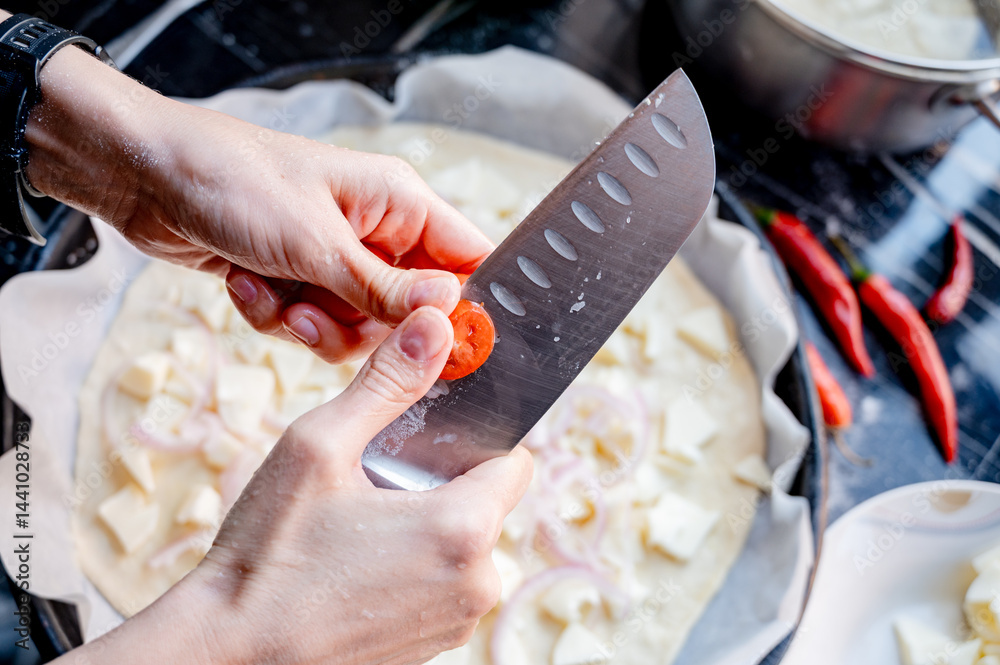 Close-up scene of female hands. Cutting tomato adding pieces of fresh tomato to dough on kitchen countertop. Making homemade pizza with three types of cheese – female hands in action.