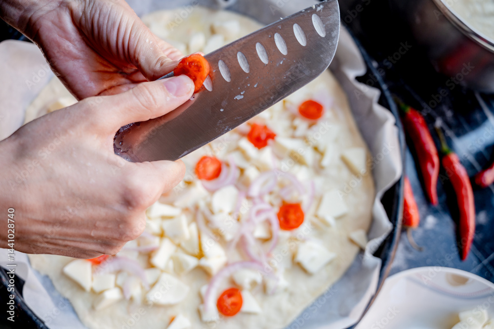 Close-up scene of female hands. Cutting tomato adding pieces of fresh tomato to dough on kitchen countertop. Making homemade pizza with three types of cheese – female hands in action.