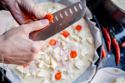 Obraz na płótnie Close-up scene of female hands. Cutting tomato adding pieces of fresh tomato to dough on kitchen countertop. Making homemade pizza with three types of cheese – female hands in action. w salonie