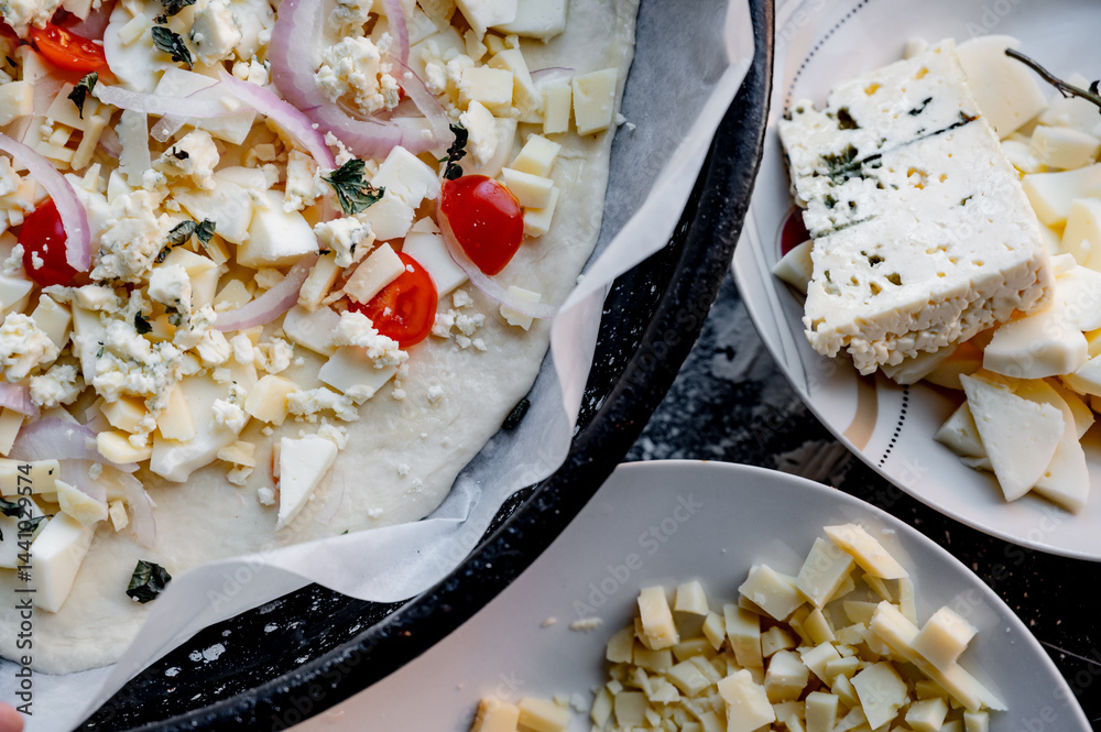 A homemade pizza in its raw form, assembled with toppings. The dough is uncooked but fully prepared with sauce, cheese, and fresh ingredients. The kitchen is cozy and softly lit, with utensils, bowls,