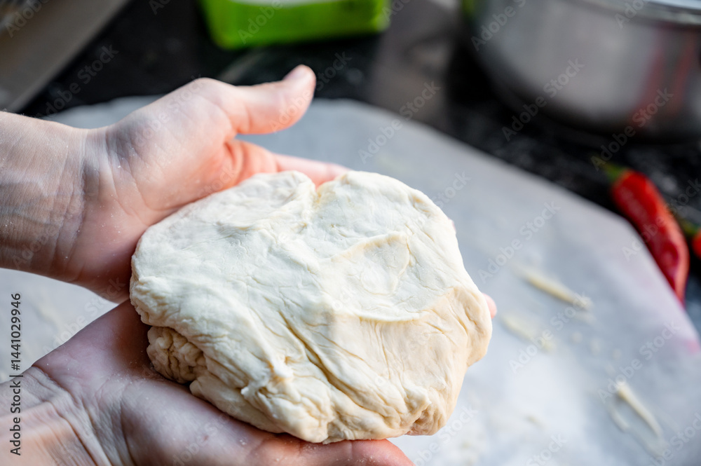 Homemade Pizza Preparation with Three Cheeses – Female Hands in Action. A warm, close-up scene of a woman’s hands preparing homemade pizza dough on a kitchen countertop. Photo recipe.
