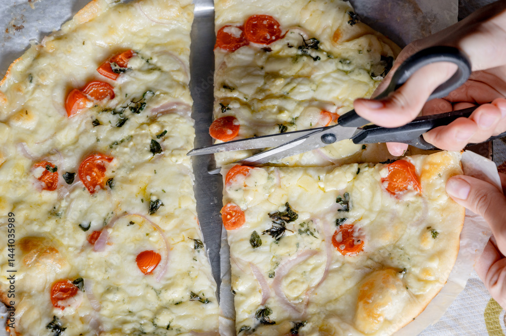 Cutting fresh homemade pizza with scissors