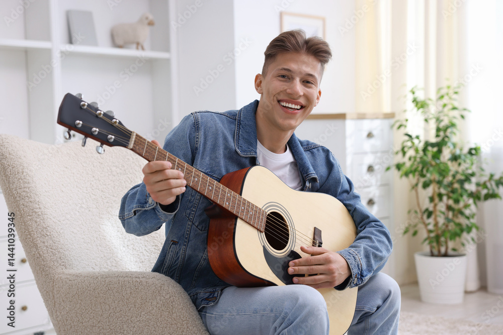 Happy man playing guitar on armchair indoors