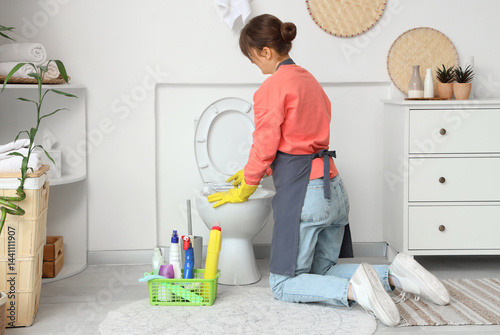 Young woman cleaning toilet...