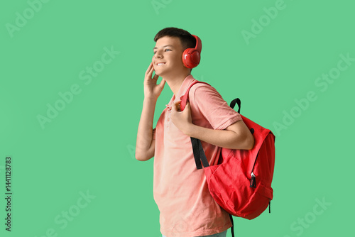 Teenage boy in headphones with backpack on green background
