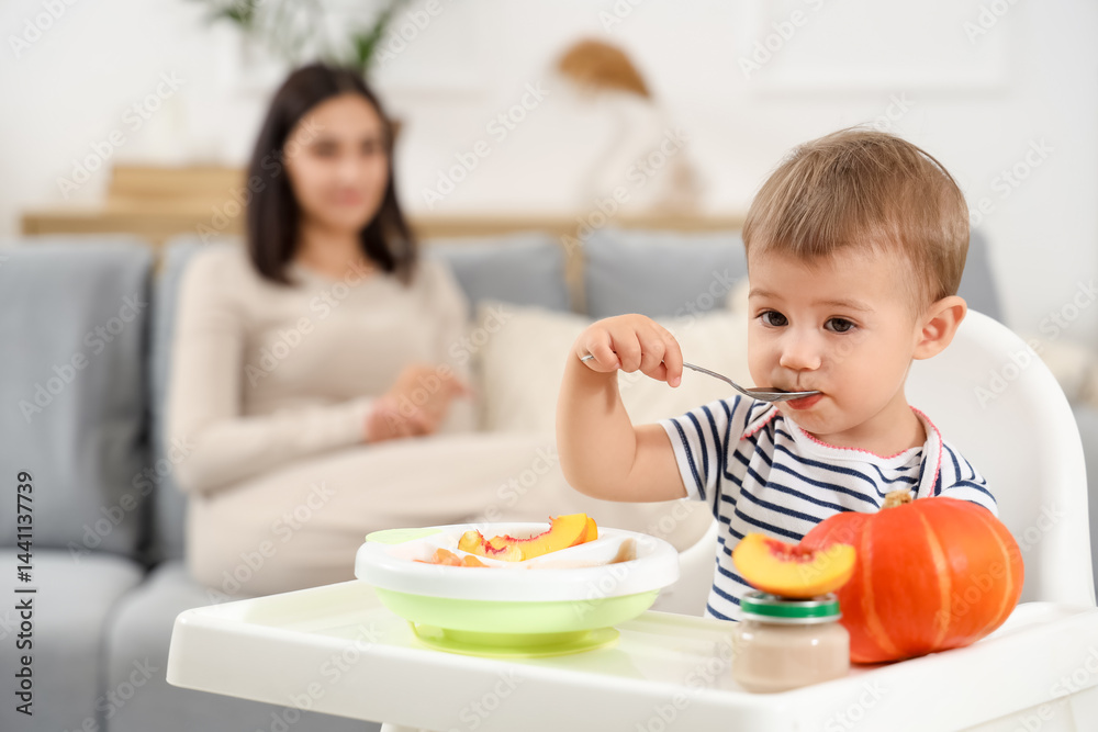Cute little baby with bowl of tasty food, fruits and vegetable eating while mother sitting on sofa at home Cute little baby with bowl of tasty food, fruits and vegetable eating while mother sitting on sofa at home