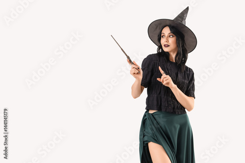 Young woman dressed as witch for Halloween with magic wand pointing at something on white background