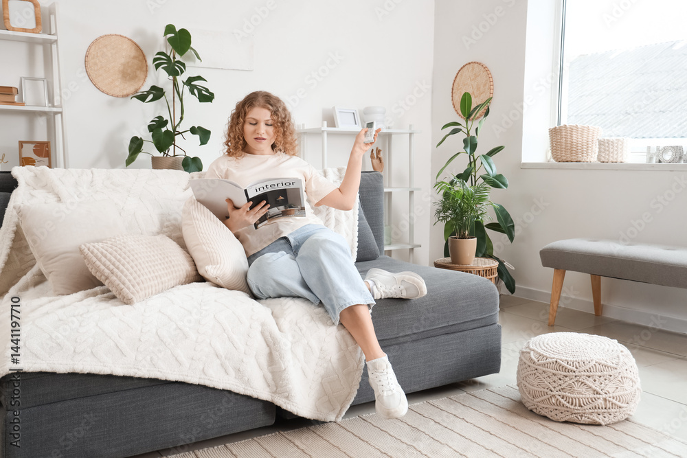 Young woman with air conditioner remote control sitting on sofa with magazine at home Young woman with air conditioner remote control sitting on sofa with magazine at home
