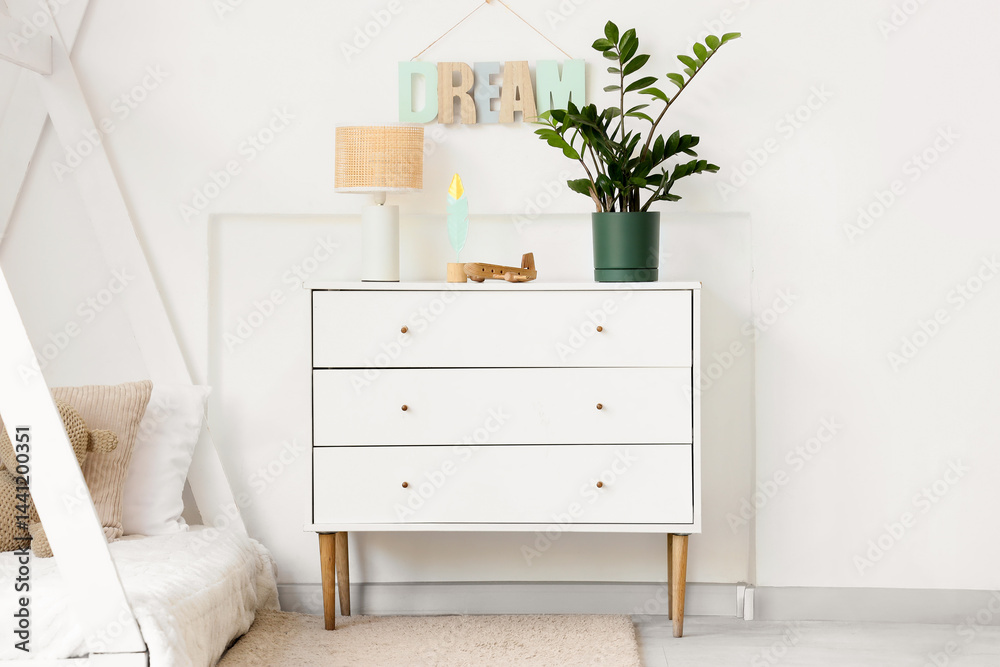 Chest of drawers with toy plane, lamp and houseplant in light nursery