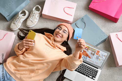 Young woman with mobile phone and credit card shopping online on carpet, top view