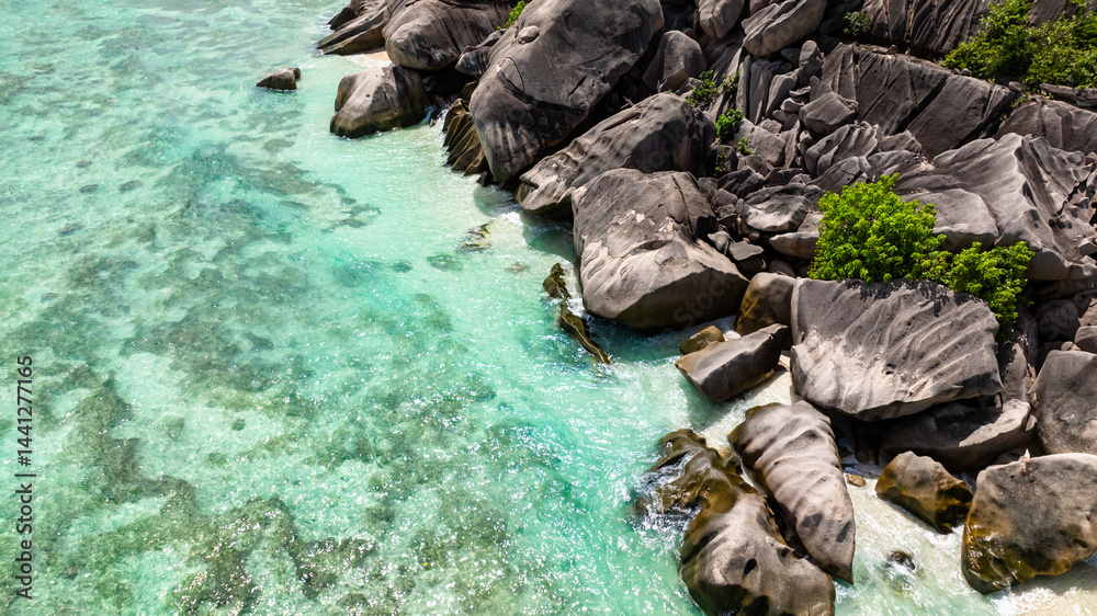 Naklejka premium Granite rocks resting on white beach as the turquoise sea gently washes over. Seychelles, La Digue.