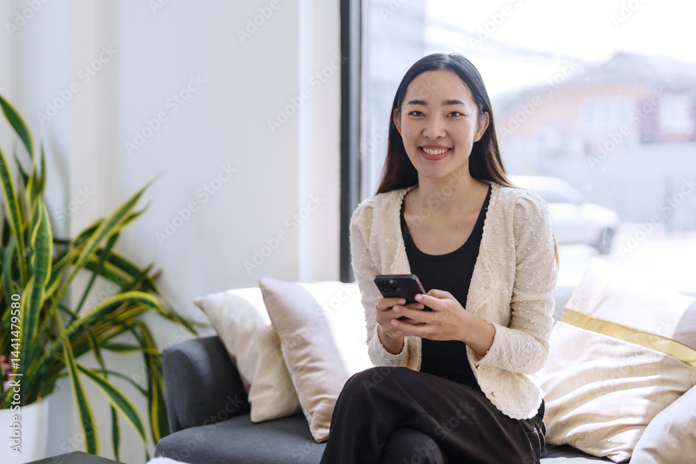 Smiling businesswoman using mobile phone while sitting on comfortable sofa in modern office space Smiling businesswoman using mobile phone while sitting on comfortable sofa in modern office space