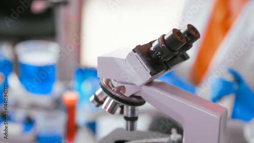 Obraz na płótnie Two Asian female scientists wearing laboratory gloves sit at a table, carefully examining a test tube filled with blue liquid, using a microscope for detailed analysis in a research laboratory w salonie