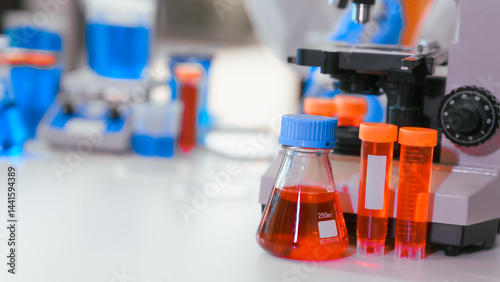 Two Asian female scientists wearing laboratory gloves sit at a table, carefully examining a test tube filled with blue liquid, using a microscope for detailed analysis in a research laboratory